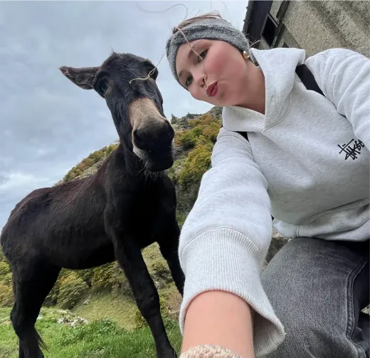 Paula macht ein Selfie neben einem Esel in einer grünen Hügellandschaft in Frankreich