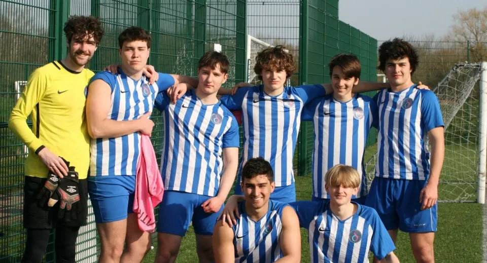 Un gruppo di giovani calciatori si trova davanti a una recinzione metallica verde nel terreno del D'Overbroeck's College.