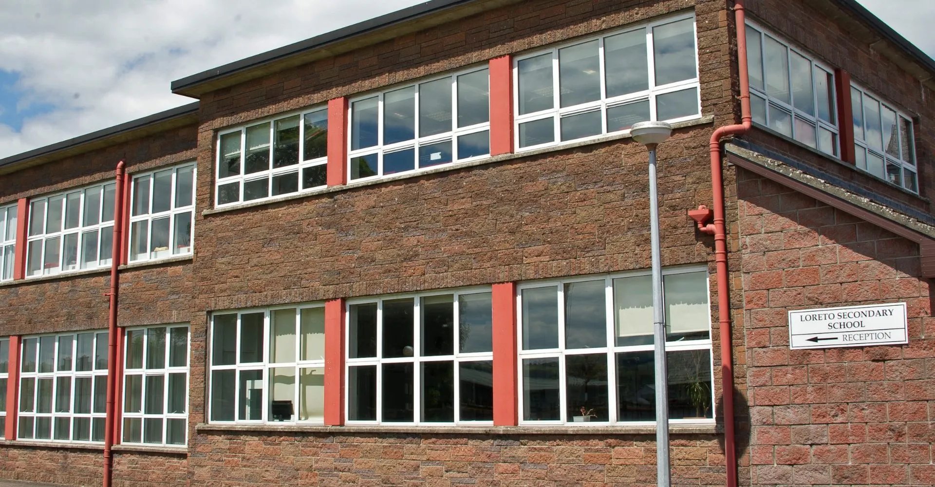 L'edificio in mattoni a più piani della Loreto Secondary School a Cork con grandi finestre e dettagli rossi sotto un cielo nuvoloso.