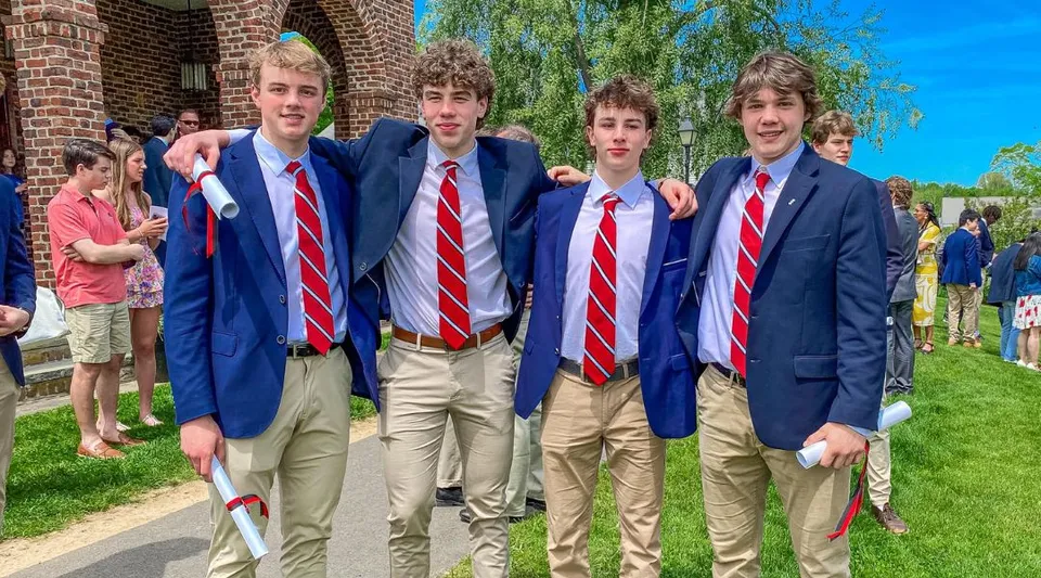 Un gruppo di studenti in giacca blu e cravatta rossa davanti a un edificio in mattoni nel campus della South Kent School.