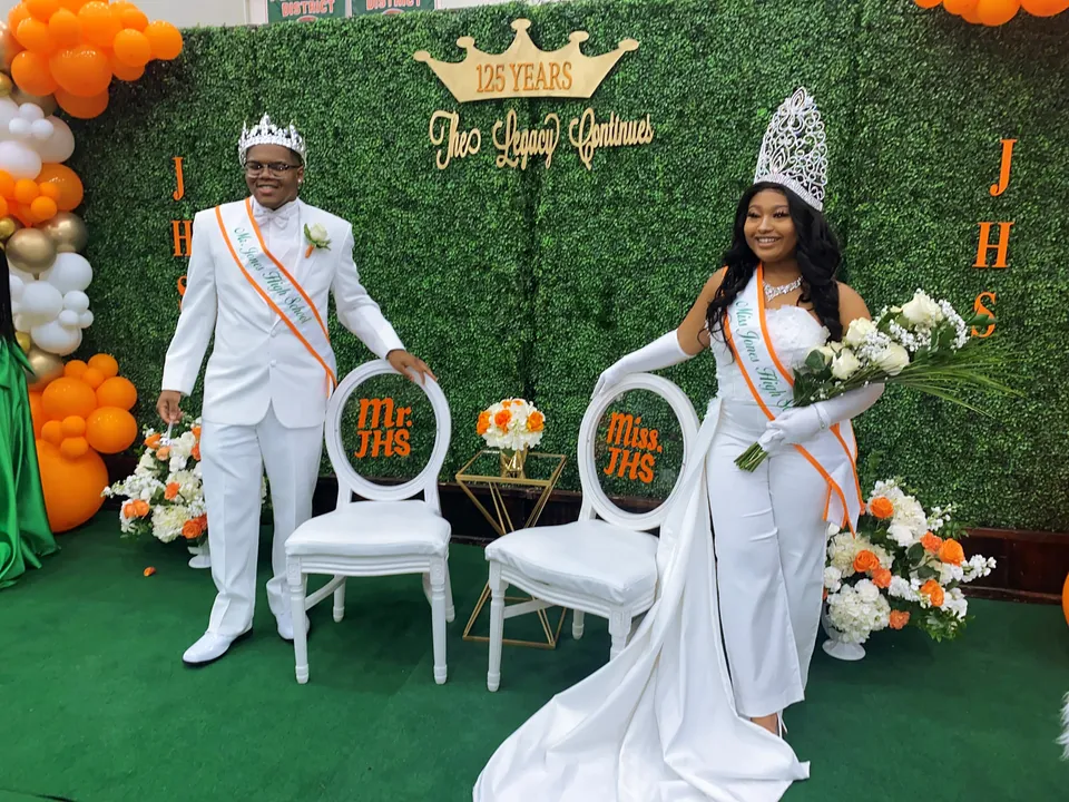 Un uomo e una donna in abbigliamento formale sono in piedi a un evento nel campus della Jones High School davanti a uno sfondo decorativo con fiori e palloncini.