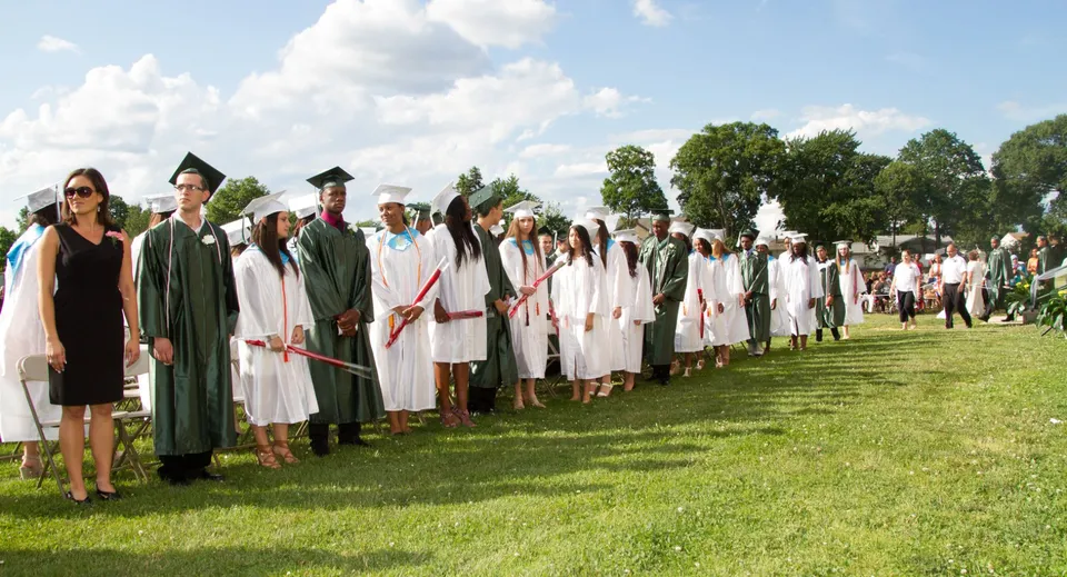 Un gruppo di neodiplomati del Provo City School District si trova su un prato con alberi e cielo nuvoloso sullo sfondo.