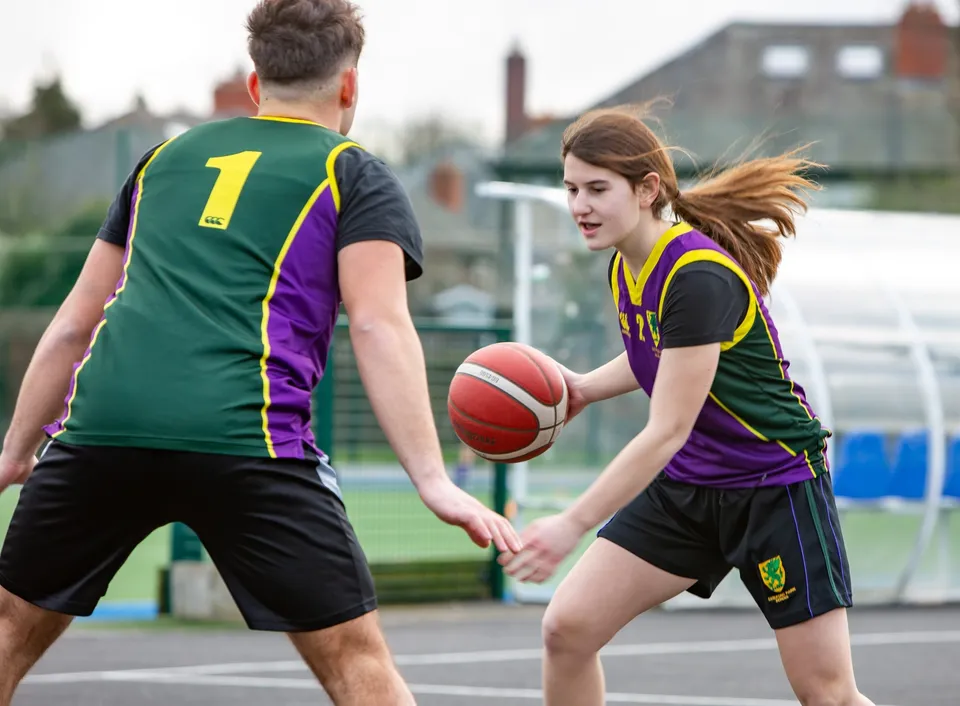 Due studenti della Sandford Park School giocano a pallacanestro su un campo all'aperto.