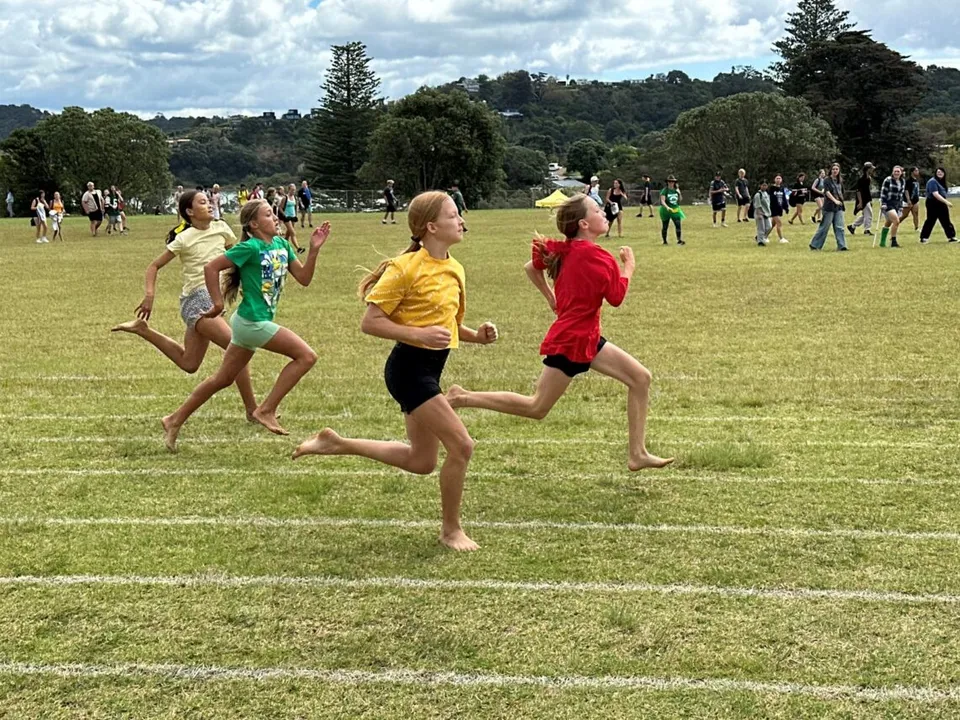 Quattro studentesse della Waiheke High School corrono a piedi nudi durante una gara su un campo d'erba.