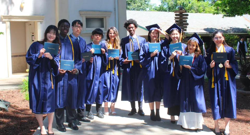 I diplomati della Canyonville Academy posano insieme in toga blu davanti a un edificio circondato da alberi.