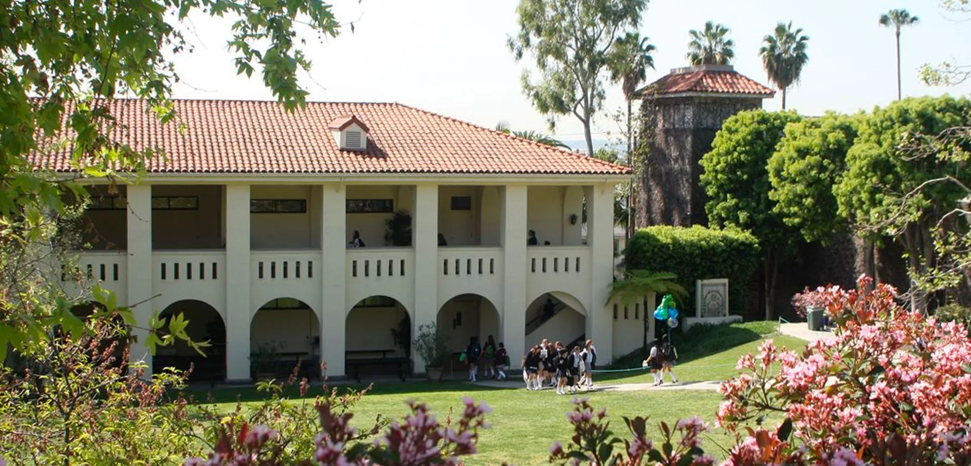 L'edificio della Immaculate Heart High School, con un tetto in tegole e porticati, è circondato da un giardino curato e fiori in fiore.