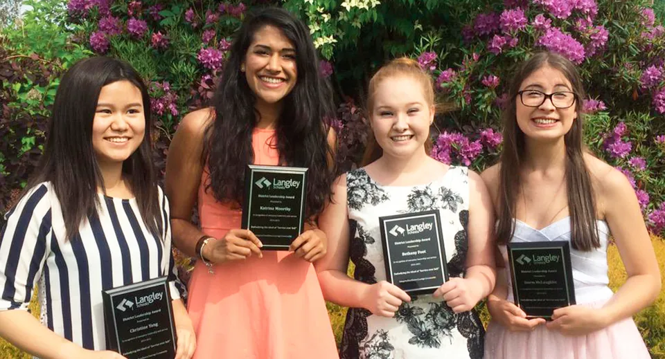 Quattro studentesse della Langley Fine Arts School sono insieme in un giardino con fiori rosa sullo sfondo.