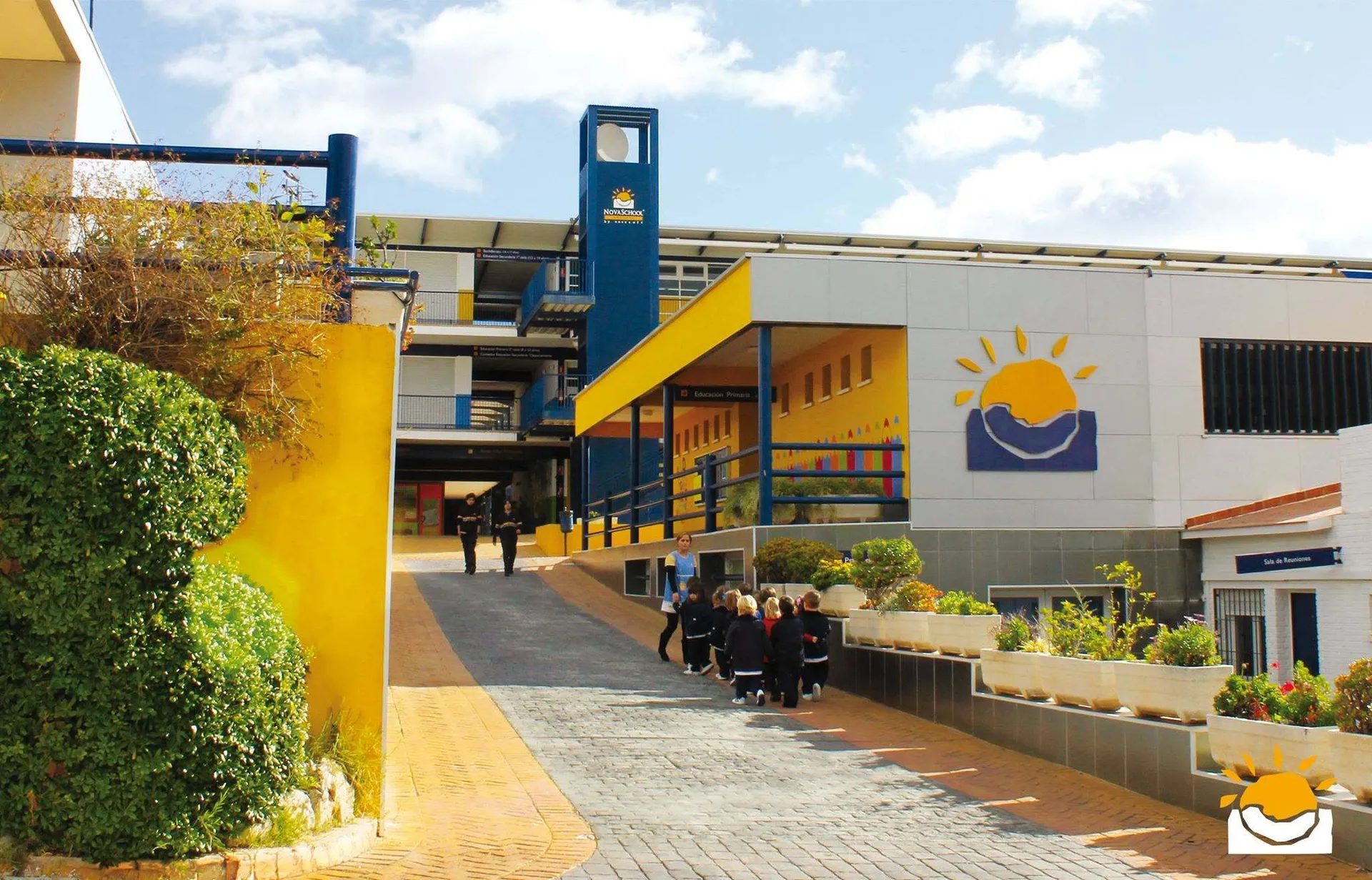 L'edificio del Novaschool Añoreta College con facciata blu e gialla e un gruppo di bambini nel campus.