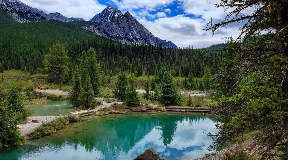 Un calmo lago di montagna riflette le cime e le foreste di abeti nel paesaggio vicino al John Taylor Collegiate.