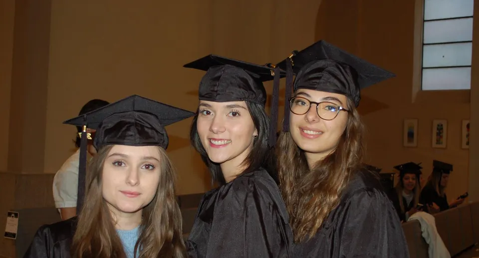 Tre studentesse in abito da diploma posano insieme nel campus del Lycée Polyvalent Philippine Duschenes.