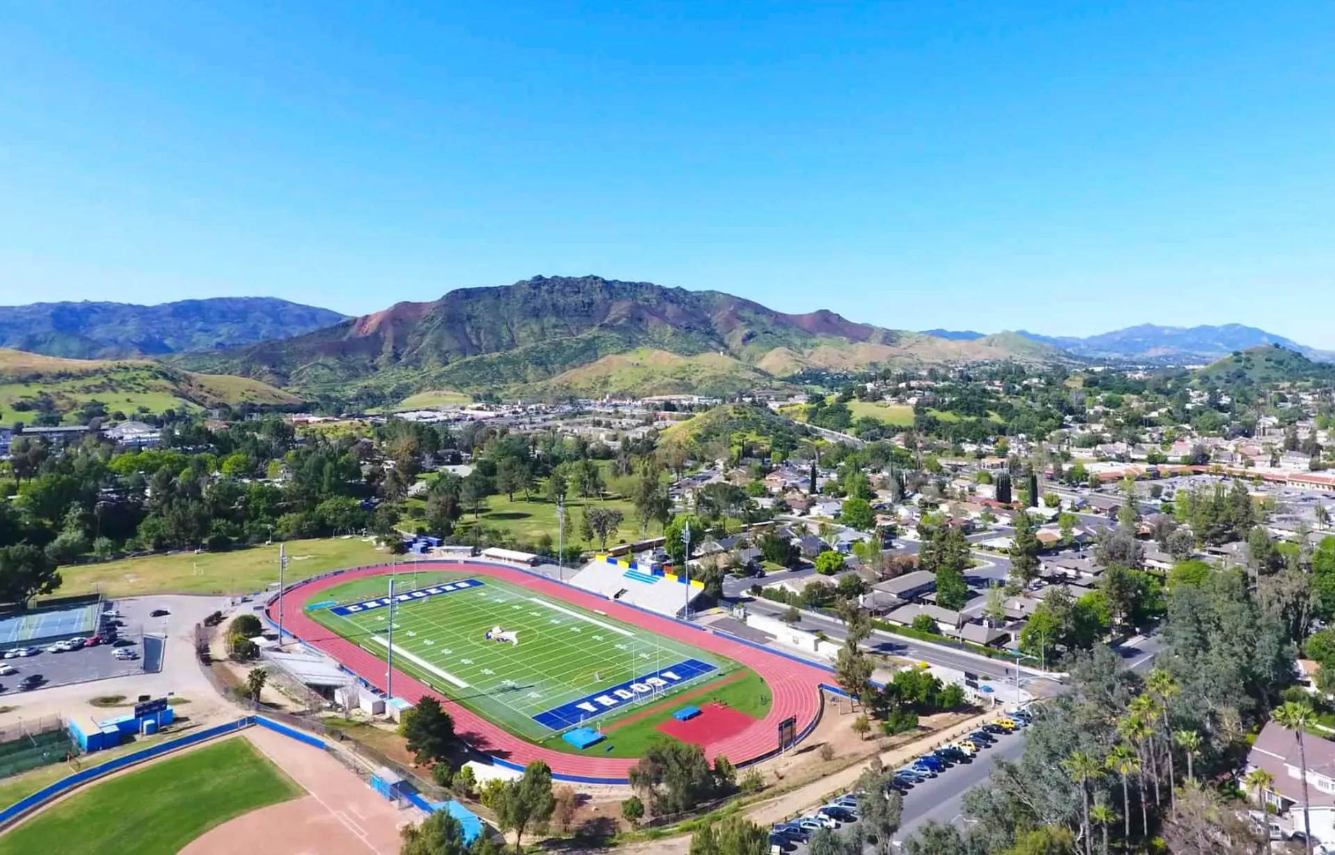 Il campo sportivo del Las Virgenes Unified School District con dintorni verdi e montagne sullo sfondo sotto un cielo azzurro.