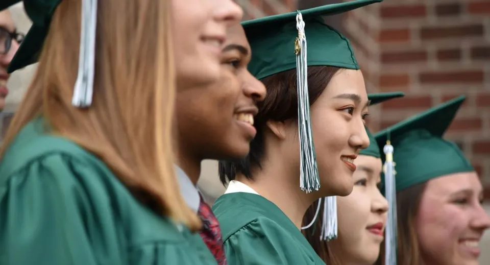 I diplomati della Boston Trinity Academy sono insieme in toga e tocco verdi e sorridono.
