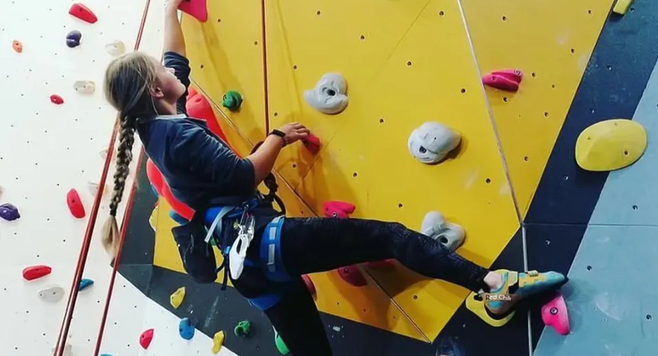 Una persona con attrezzatura da arrampicata scala la parete d'arrampicata colorata nel campus del Malvern College.