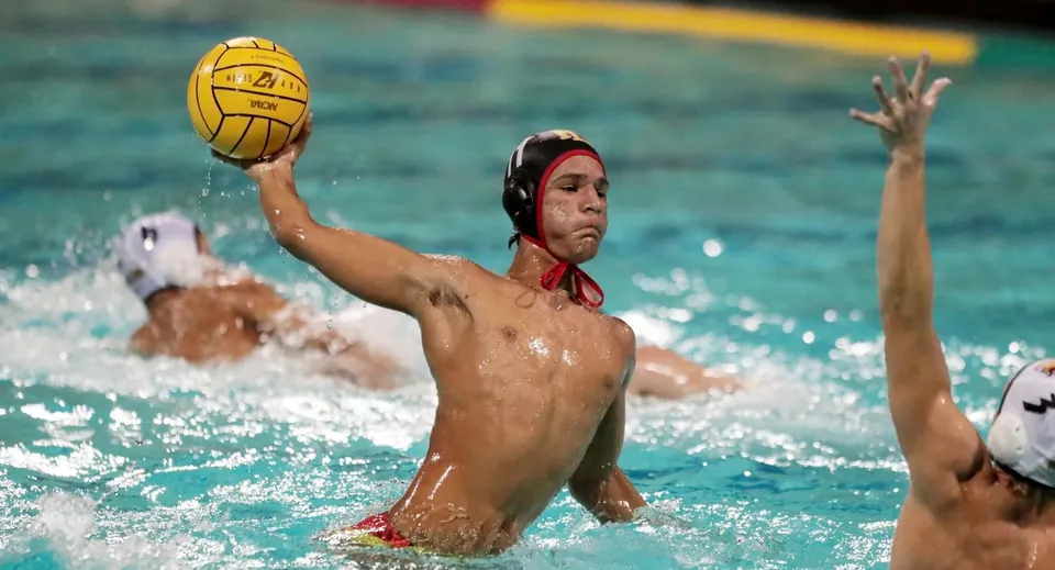Un giocatore del Radley College con la cuffia rossa colpisce la palla gialla durante una partita di pallanuoto.