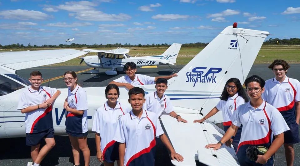 Studenti della Morley Senior High School in divisa bianca e rossa posano davanti al piccolo aereo Sky Hawk su un prato.