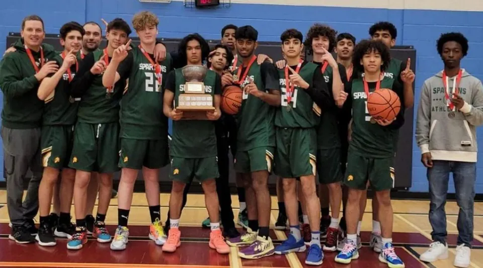 Un gruppo di studenti della Craig Kielburger Secondary School in posa con un trofeo di pallacanestro nella palestra.