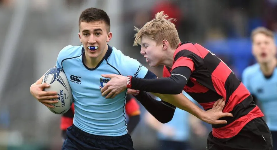 Due giocatori di rugby lottano sul campo del St. Michael's College, uno indossa una maglia azzurra e l'altro una rosso-nera.