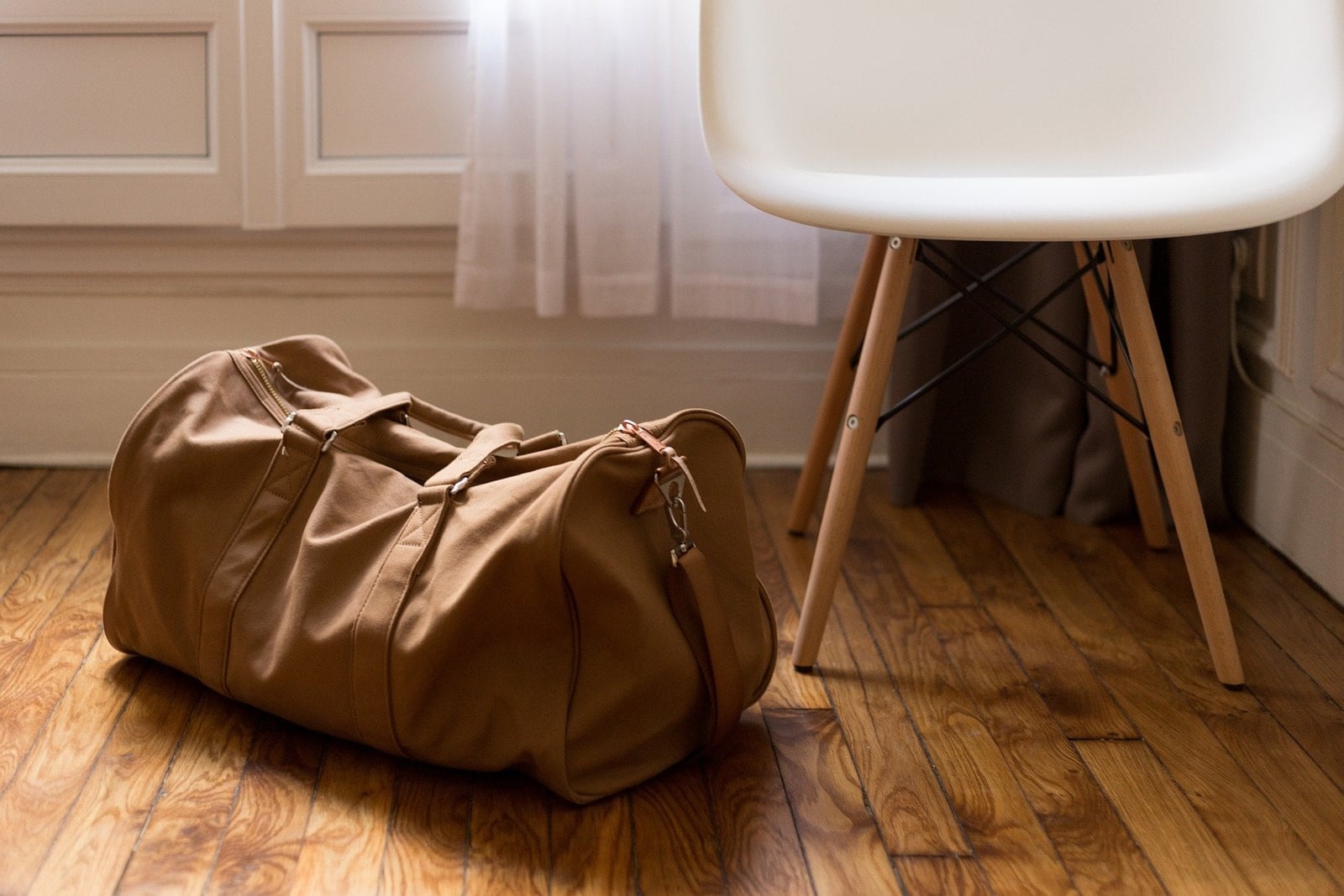 Braune Reisetasche auf dem Holzboden neben einem weißen Stuhl