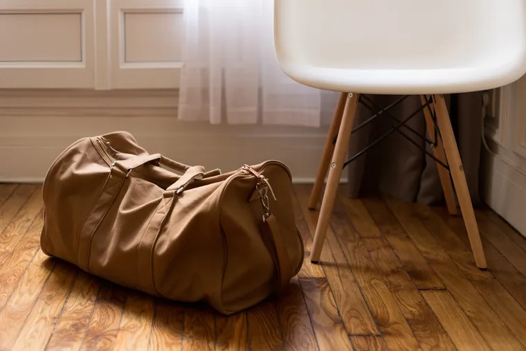 Braune Reisetasche auf dem Holzboden neben einem weißen Stuhl