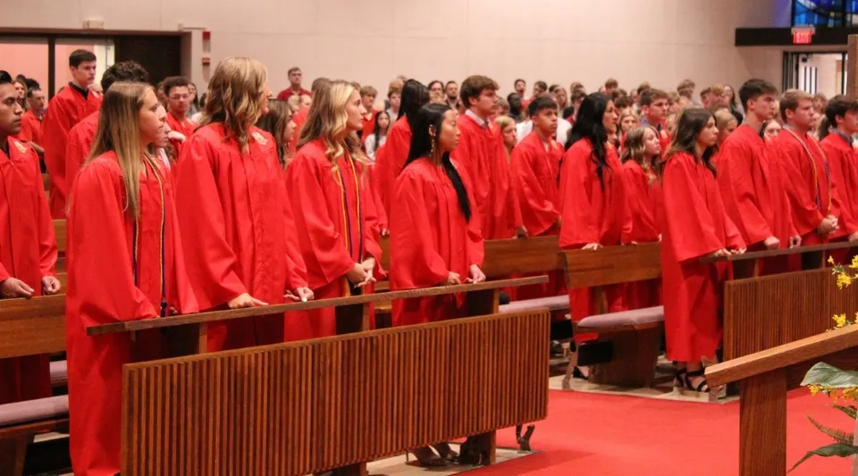 Studenti della Kuemper Catholic High School indossano toghe rosse e siedono in un ambiente simile a una chiesa.