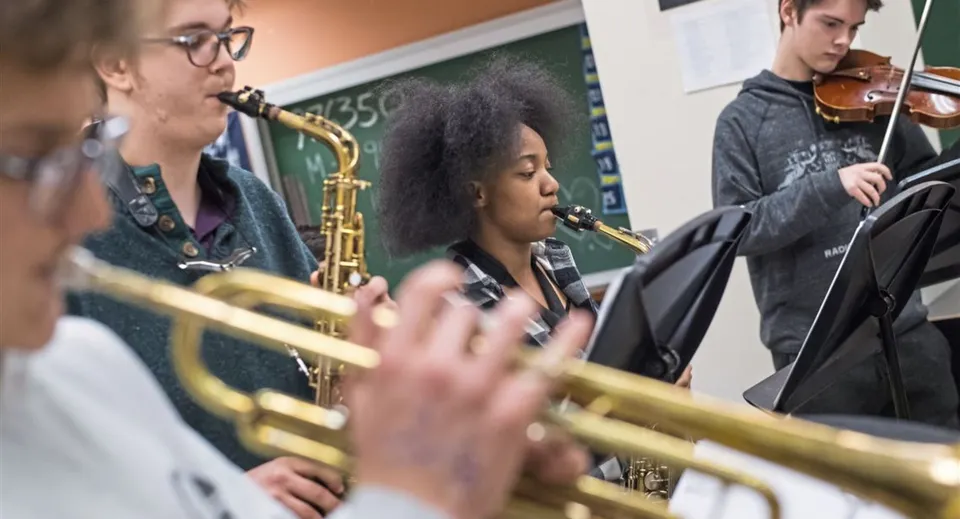 Studenti del Clovis Unified School District suonano diversi strumenti come il sassofono e il violino durante la lezione di musica in un'aula.