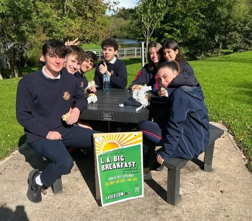Grupo de alumnos con uniforme desayunando juntos en una mesa de pícnic del jardín del colegio