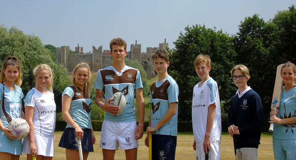 Un gruppo di studenti in divisa sportiva si trova sul campo da gioco del Framlingham College con la città sullo sfondo.