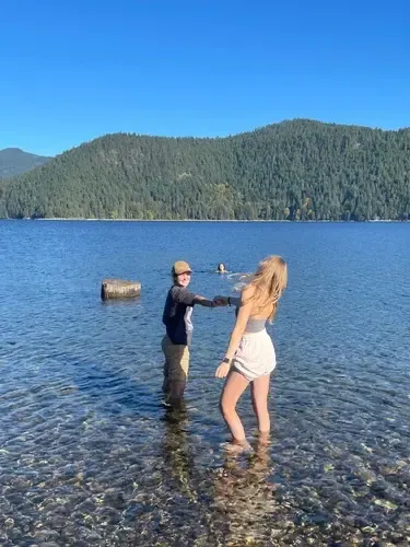 Dos jóvenes jugando en el agua poco profunda de un lago rodeado de colinas boscosas