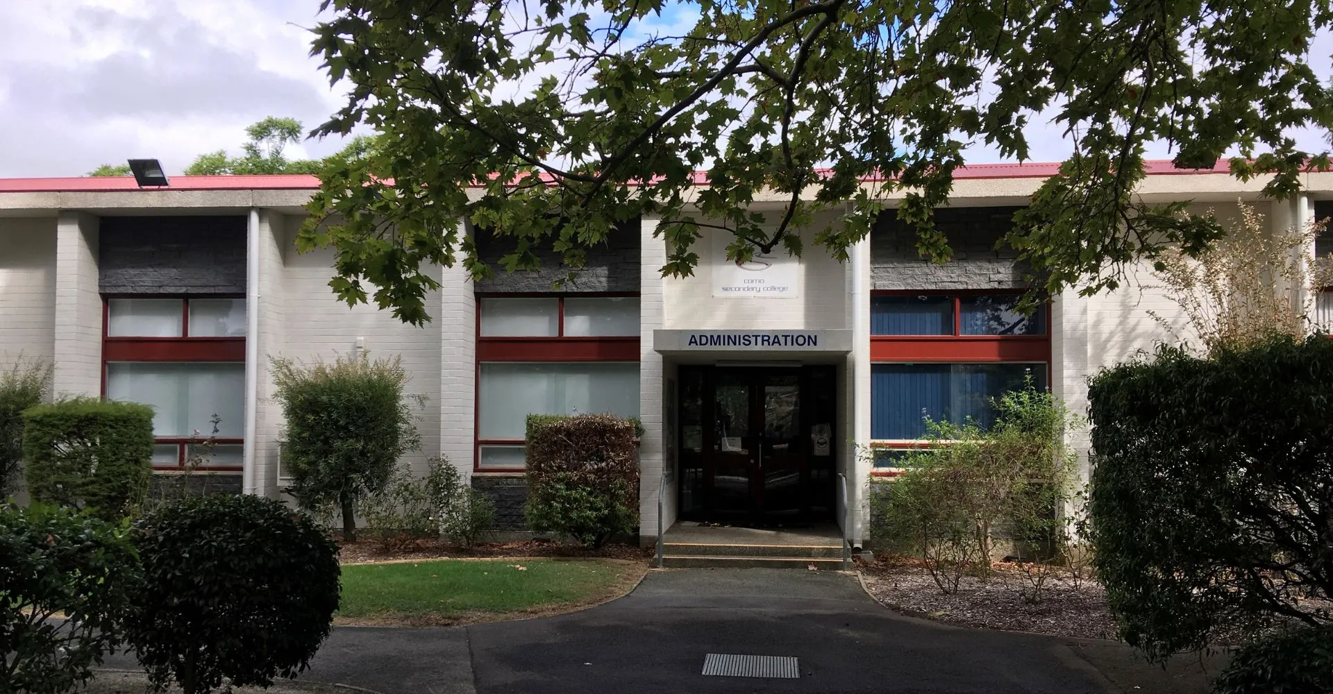 L'edificio amministrativo con tetto rosso e area d'ingresso nel campus del Como Secondary College è circondato da alberi.