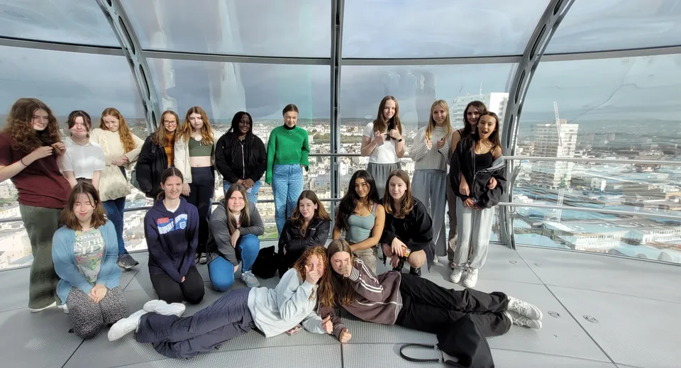 Un gruppo di studentesse della Brighton Girls School posa insieme in una stanza vetrata con vista sulla città.