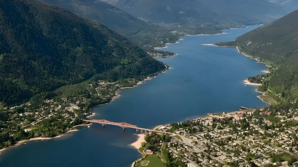 Una vista aerea mostra un lago con un ponte e montagne boscose nei dintorni della École des Sentiers-Alpins.