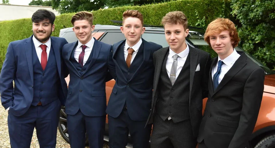 Studenti del Franciscan College Gormanston in abbigliamento formale davanti a un'auto circondata da una verde vegetazione.