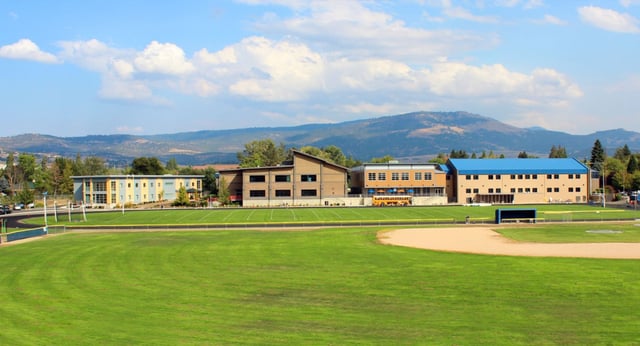 Ein grünes Feld vor dem modernen Gebäudekomplex auf dem Campus der St. Mary's School mit Bergen im Hintergrund.
