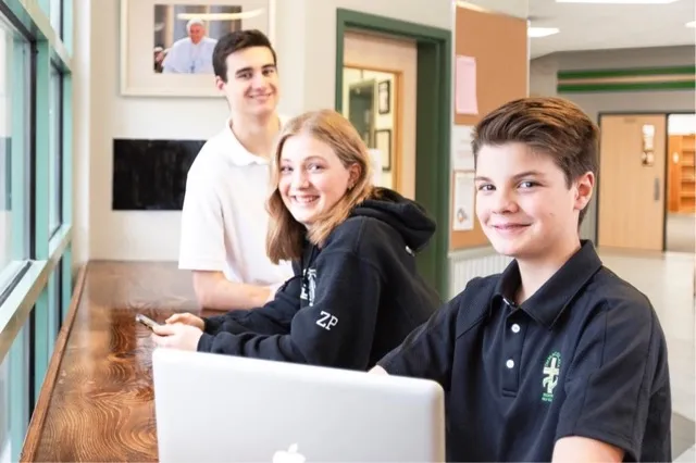 Tres estudiantes de la Immaculata Regional School están juntos sonriendo en un vestíbulo.