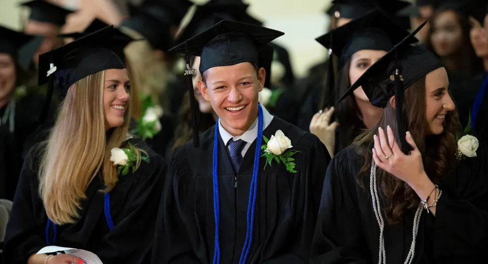 Studenti del Pickering College sorridono indossando tocco e toga neri con una rosa bianca alla cerimonia di diploma.