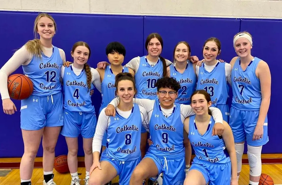 Un gruppo di studentesse in divisa da basket blu posa davanti a una parete blu nel campus della Catholic Central High School.