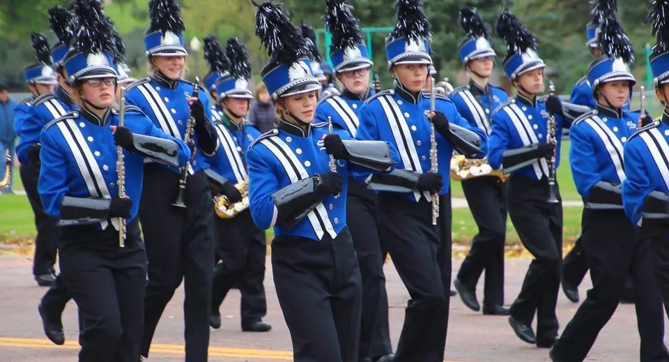 I membri della Marching Band della Sioux Falls Christian School in uniforme blu e nera su un prato con alberi sullo sfondo.