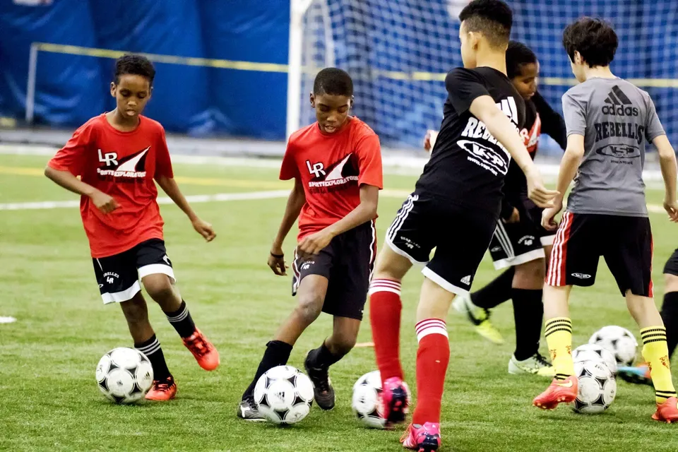 Un gruppo di giovani calciatori con maglie rosse e nere gioca sul campo sportivo delle Eastern Ontario Public Schools.
