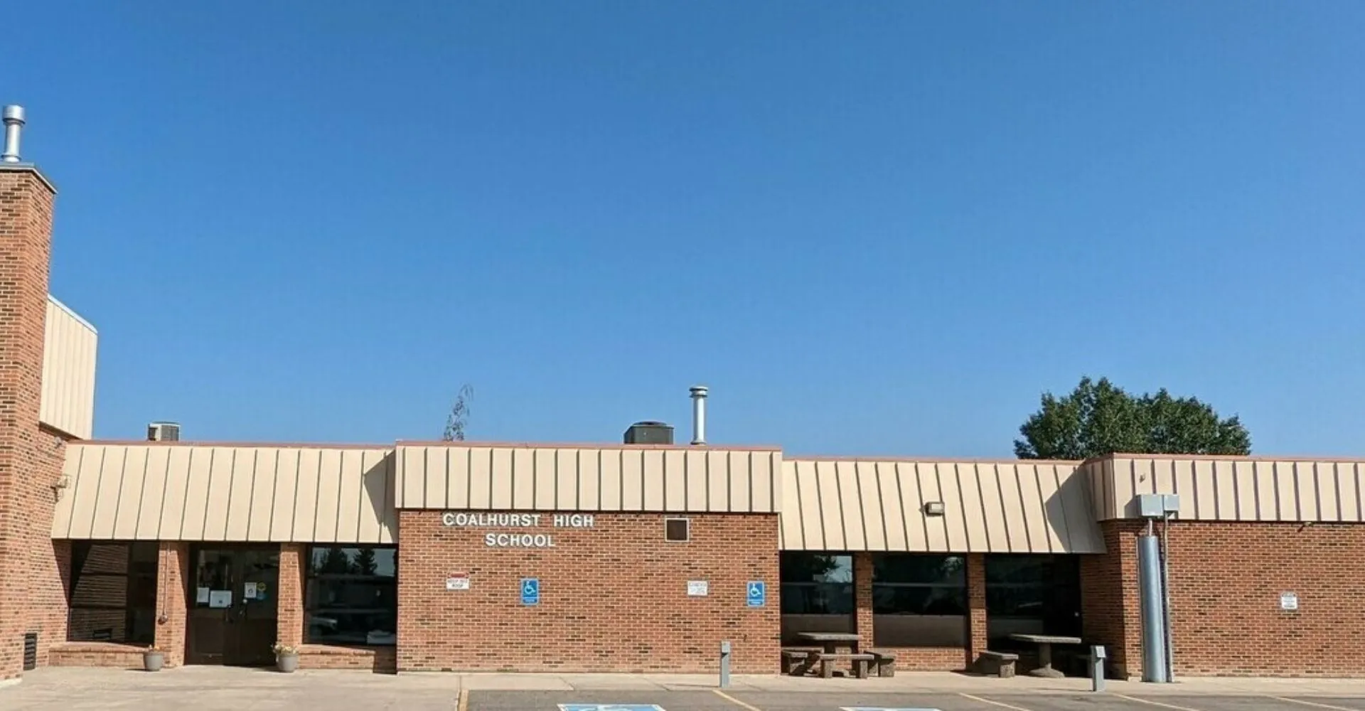 L'edificio in mattoni della Coalhurst High School si trova circondato da alberi sotto un cielo azzurro e limpido.