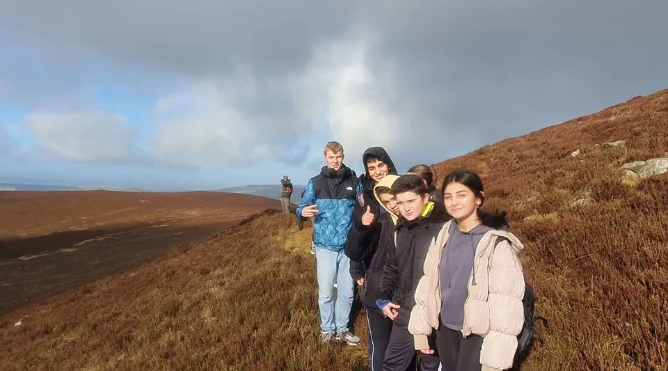 Un gruppo di giovani del Duiske College si trova su una collina sotto un cielo nuvoloso.