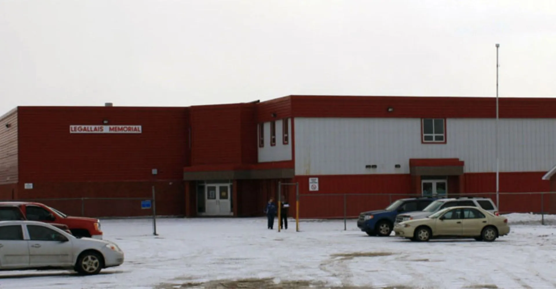L'edificio in mattoni rossi della St. James' Regional High si trova davanti a un parcheggio innevato con veicoli parcheggiati.