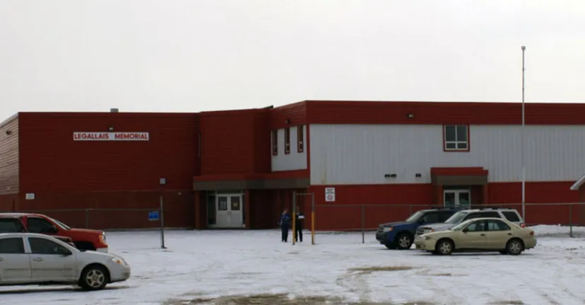 L'edificio in mattoni rossi della St. James' Regional High si trova davanti a un parcheggio innevato con veicoli parcheggiati.