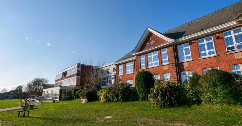 L'edificio in mattoni a più piani dell'Itchen Sixth Form College con un'ampia vetrata di fronte a un prato e alberi è visibile sotto un cielo limpido.