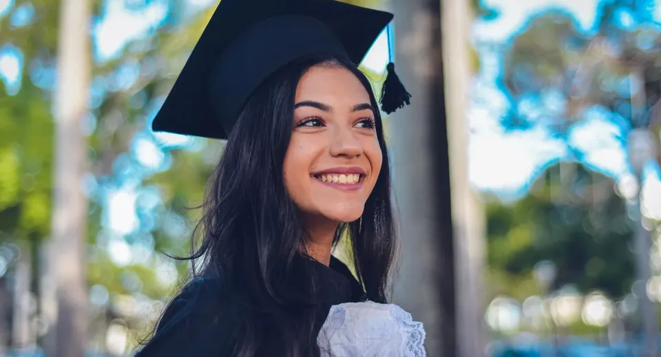 Una giovane donna in abito da diploma si trova davanti a uno sfondo naturale nel campus della Matthew Halton High School.