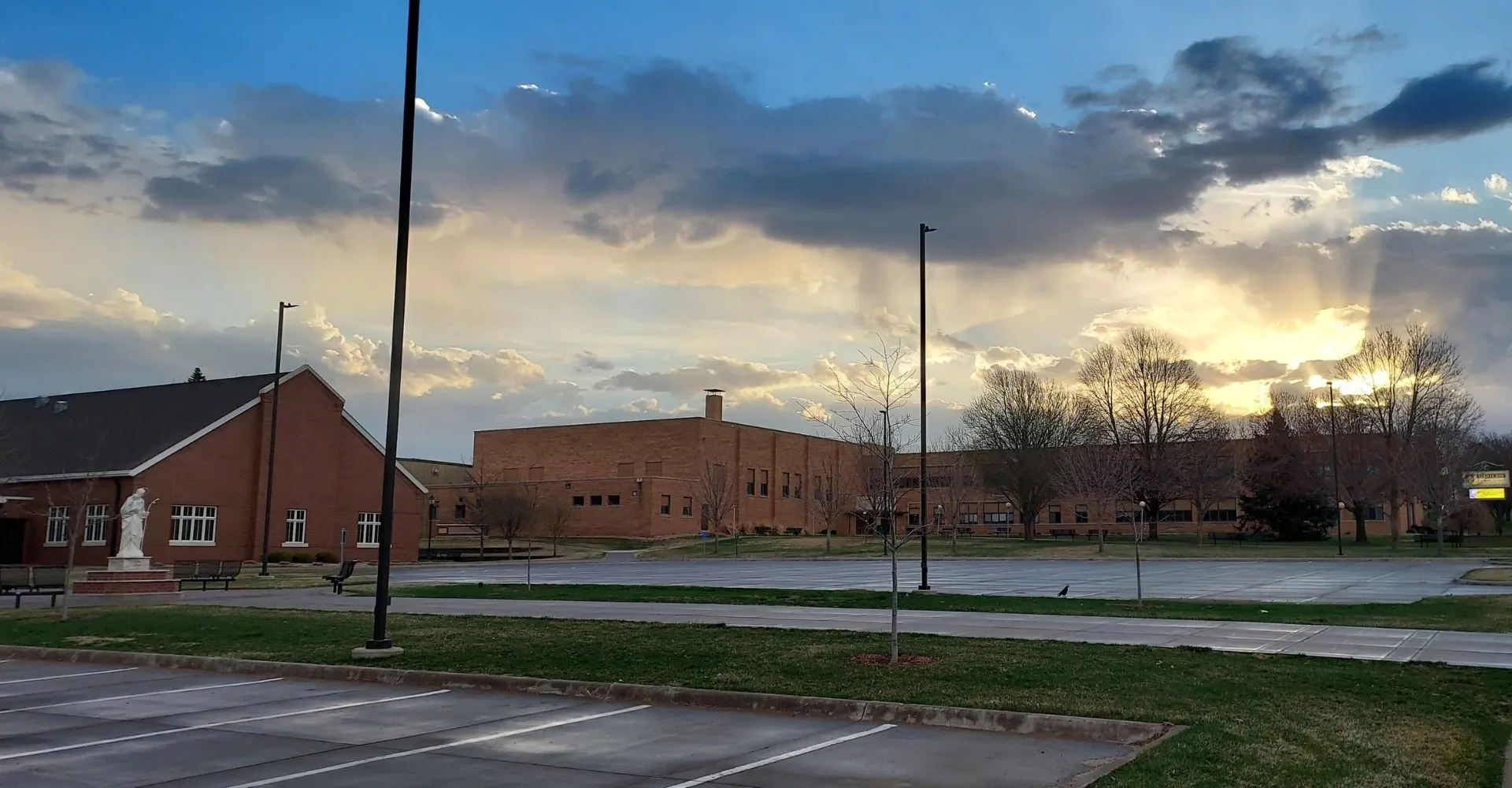 Si vede l'edificio in mattoni della Gehlen Catholic School con un prato in primo piano e un tramonto colorato sullo sfondo.