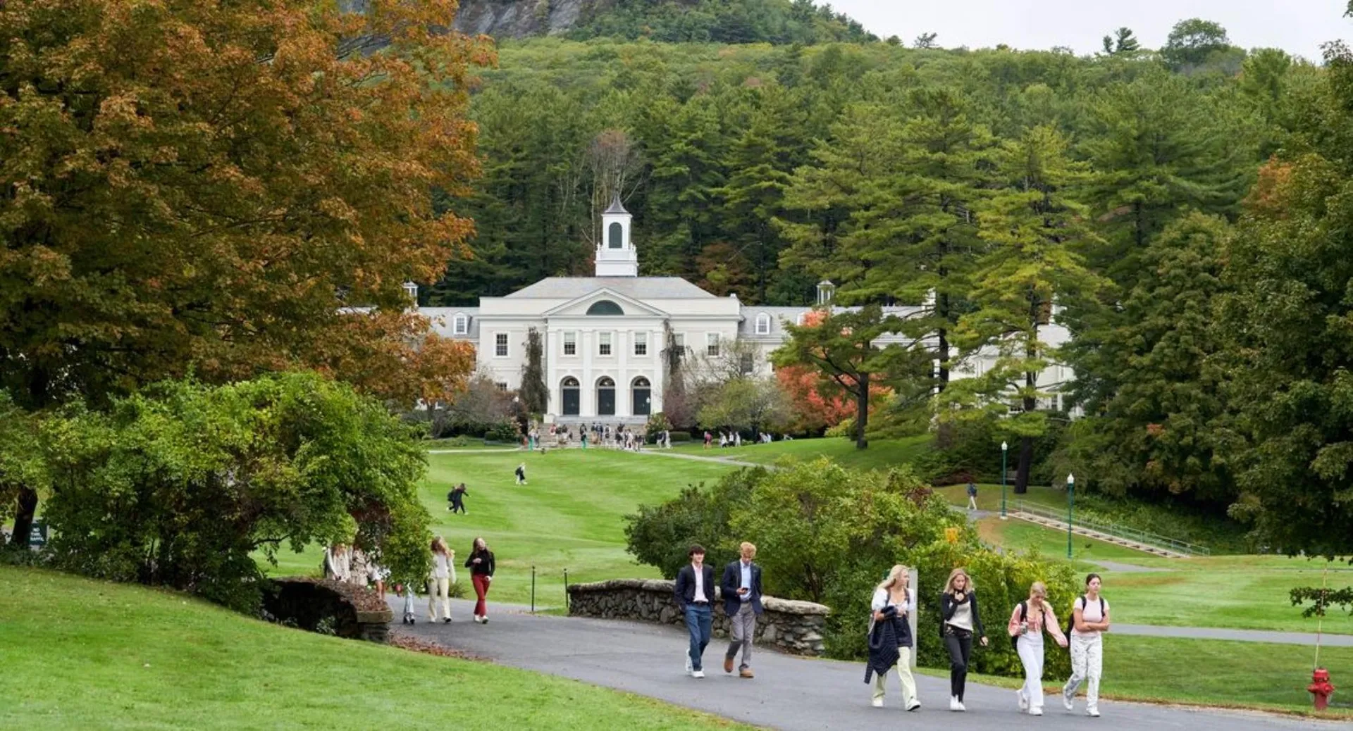 Il campus della Berkshire School mostra un edificio storico circondato da alberi autunnali e persone a passeggio su viali ben tenuti.