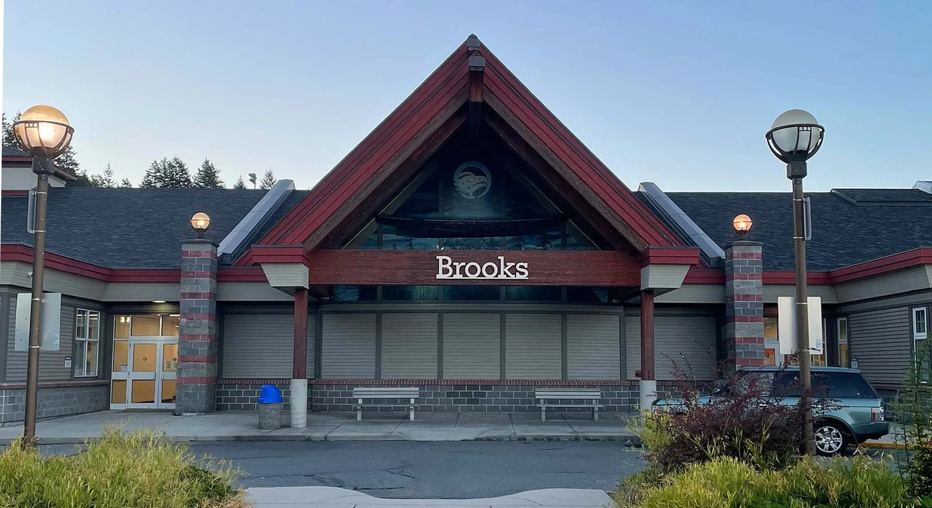 L'edificio principale a forma triangolare della Brooks Secondary School è circondato da un'area pavimentata e spazi verdi sotto un cielo limpido.
