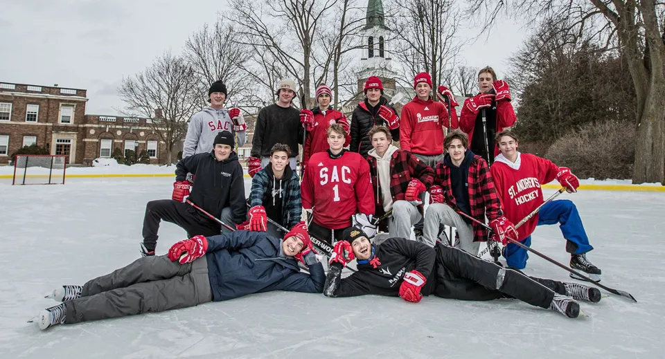 Un gruppo di studenti del St. Andrew’s College si raduna su una pista da ghiaccio con lo sfondo di un campanile.