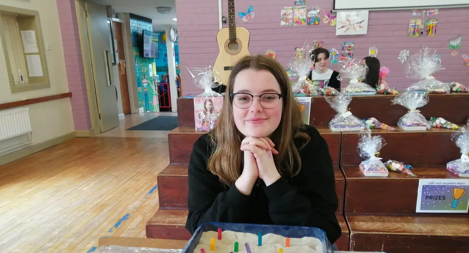 Una studentessa della St. Louis Secondary School sorride seduta a un tavolo davanti a gradini in legno con regali confezionati.
