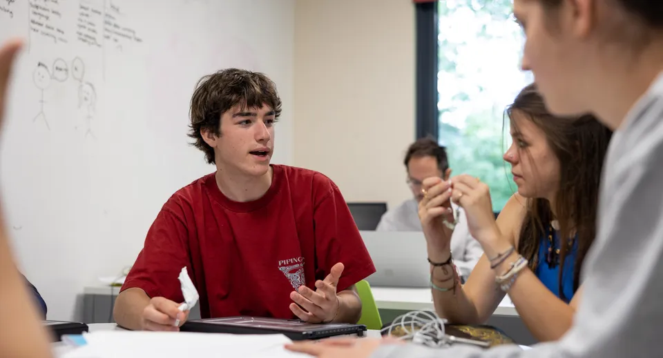 Uno studente del Wellington College discute in classe con altre due persone davanti a una lavagna bianca.